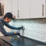 A man installing an electrical outlet in a kitchen.